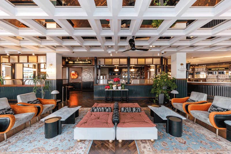 Hotellobby mit zentralen Tagesbetten, bunten Sesseln, Teppichen und Bar im Hintergrund.
