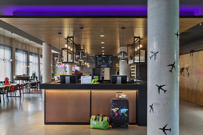 Rezeption eines Hotels mit Tresen, zwei Koffern davor, Sitzbereich links und Säule mit Flugzeugmotiven.