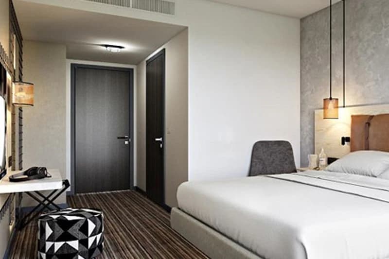Hotelzimmer mit Doppelbett, Nachttischlampen, Schreibtisch, Telefon und zwei dunklen Türen.