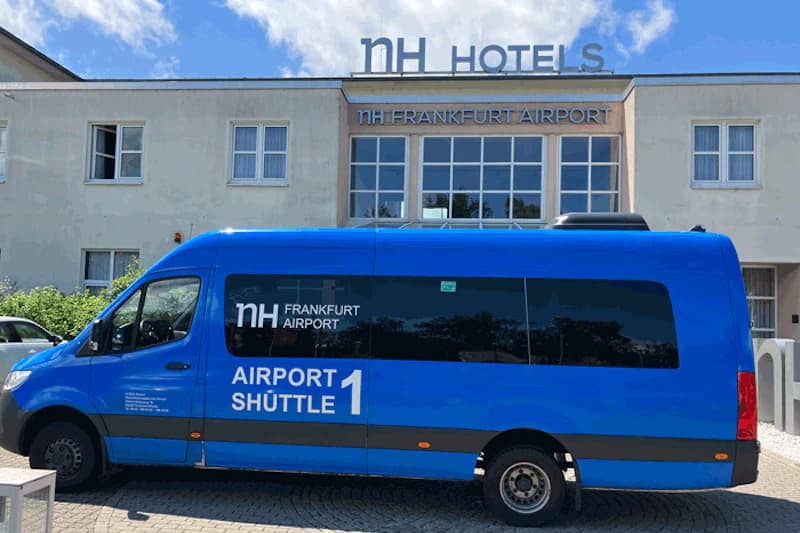 Blauer Shuttlebus vor dem Haupteingang des NH Frankfurt Airport am Flughafen Frankfurt.