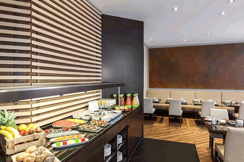 Frühstücksbuffet mit Obst, Gebäck, Aufschnitt, Säften und gedeckten Tischen im Hotelrestaurant.