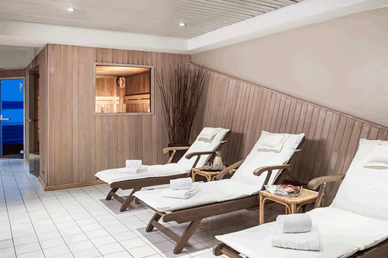 Ruheraum mit Liegen, Handtüchern und Fenster zur Sauna.