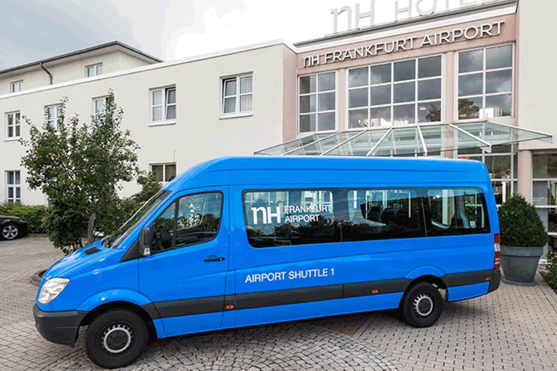 Blauer Shuttlebus vor dem Haupteingang des NH Frankfurt Airport mit Glasvordach.