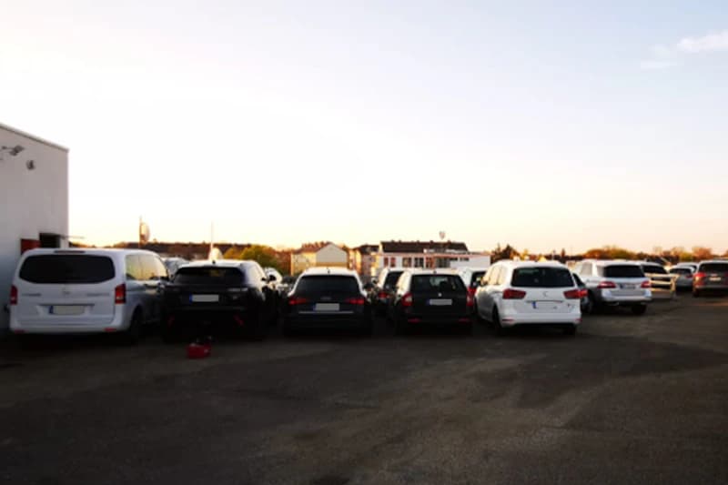 Mehrere geparkte Autos von hinten auf offenem Asphaltparkplatz neben einem Gebäude bei Sonnenuntergang.