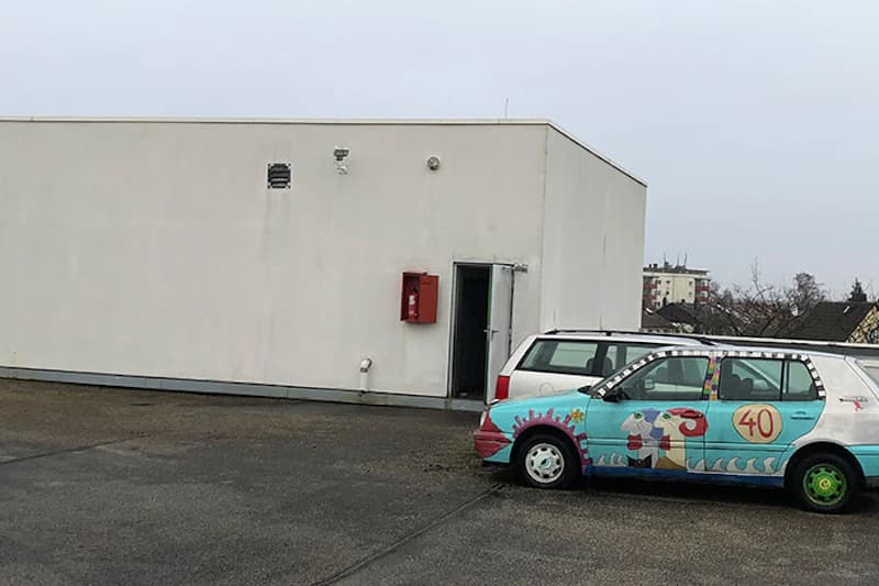 Flache Dachfläche mit kleinem weißem Technikgebäude und zwei parkenden Autos, eines bunt bemalt mit Zahl 40.