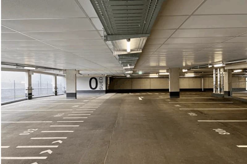 Leeres Parkdeck mit markierten Stellplätzen, Deckenlampen, Pfeilmarkierungen und Wandbeschriftung 0 Süd.