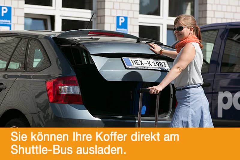 Frau lädt Koffer in geöffneten Kofferraum eines grauen Kombiwagens auf Parkplatz vor Parkzeichen.