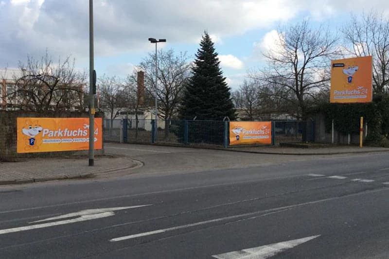 Einfahrt mit geschlossenem Metalltor und orangefarbenen Parkfuchs24-Bannern am Straßenrand.