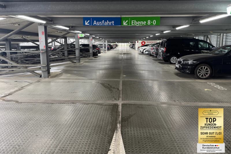 Mehrstöckiges Parkhaus mit Metallboden, geparkten Autos rechts und Schildern Ausfahrt sowie Ebene 8-0.