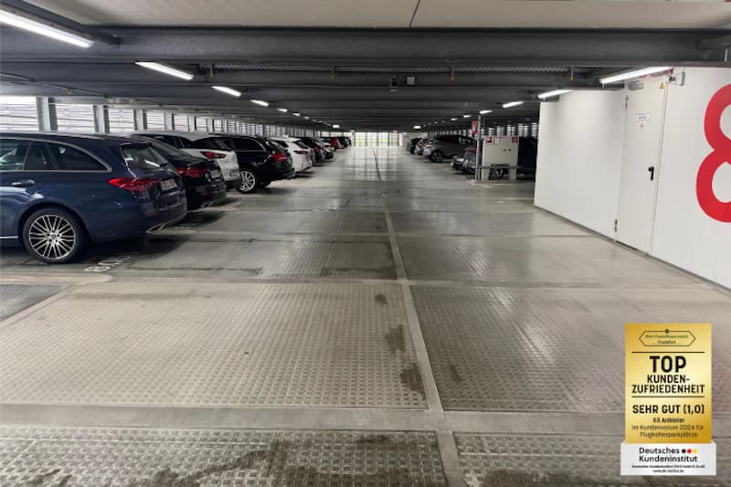 Überdachtes Parkdeck mit geparkten Autos links und rechts, beleuchteter Mittelgang und rote Acht an der Wand.