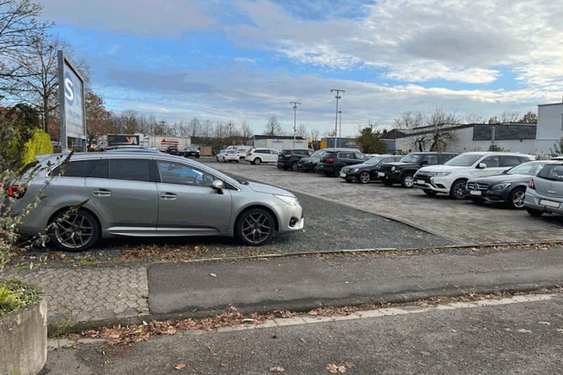 Großer Parkplatz mit mehreren geparkten Autos, Leuchtenmasten und Zufahrtschild.