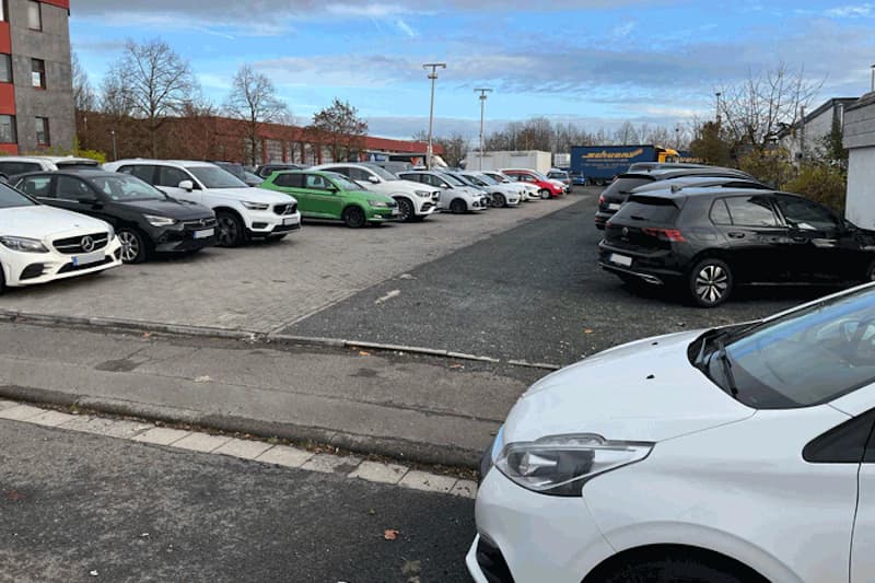 Außenparkplatz mit zwei Reihen geparkter Autos und Laternen unter bewölktem Himmel.