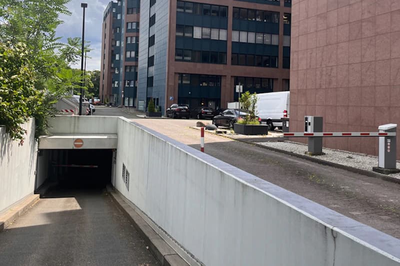 Abwärts führende Rampe zu einer Tiefgarageneinfahrt mit Sperrschild, rechts Schranke und Bürogebäude im Hintergrund.