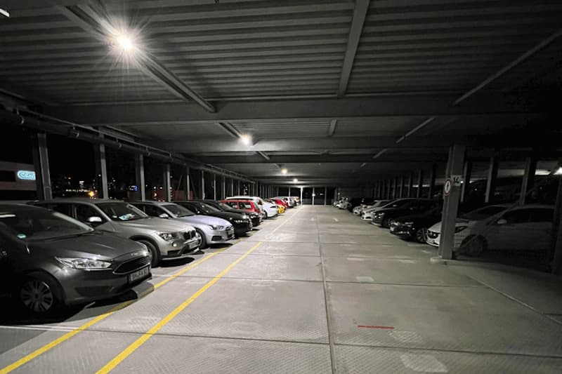 Überdachtes Parkdeck mit zwei Reihen geparkter Autos und Deckenbeleuchtung bei Nacht.