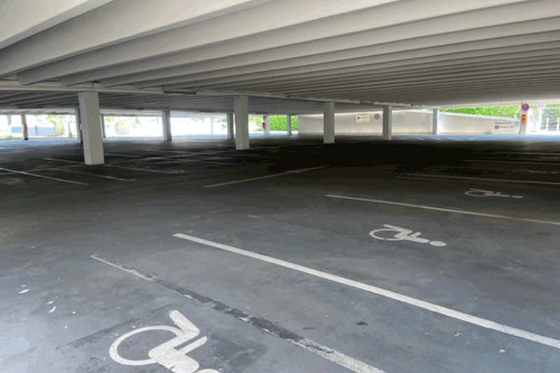 Leeres überdachtes Parkdeck mit Stützen und mehreren markierten Behindertenparkplätzen.