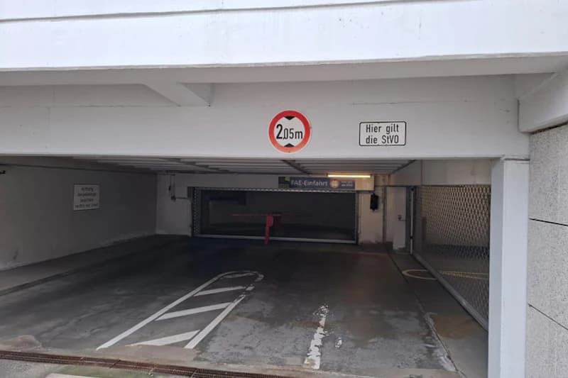Einfahrt in eine Tiefgarage mit Höhenbegrenzungsschild 2,05 m, Schranke und Fahrbahnmarkierungen.