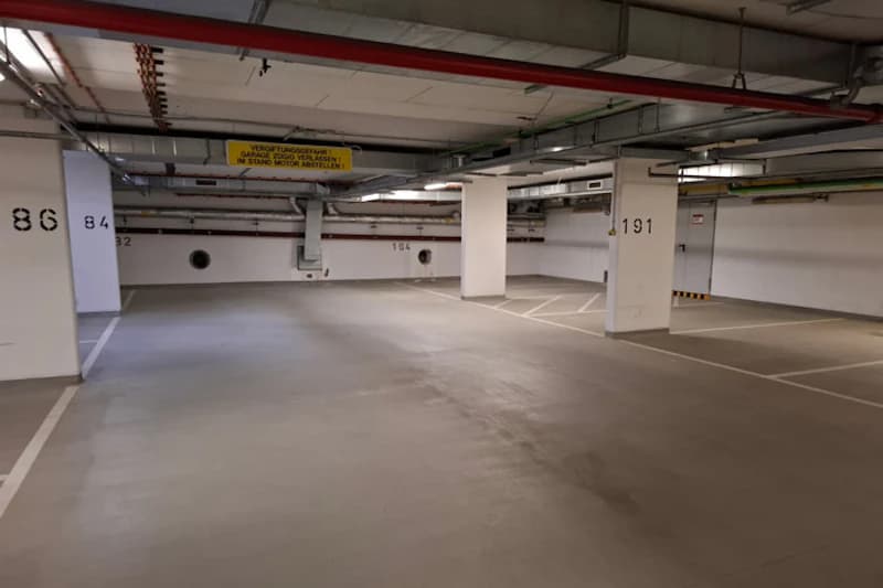 Leere Tiefgarage mit markierten Parkflächen, Stützsäulen mit Zahlen und sichtbaren Deckenleitungen.