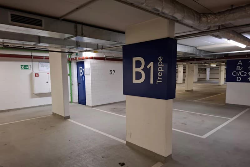 Unterirdische Tiefgarage mit Säule und blauem Schild B1 Treppe, markierte Parkflächen und blaue Tür.