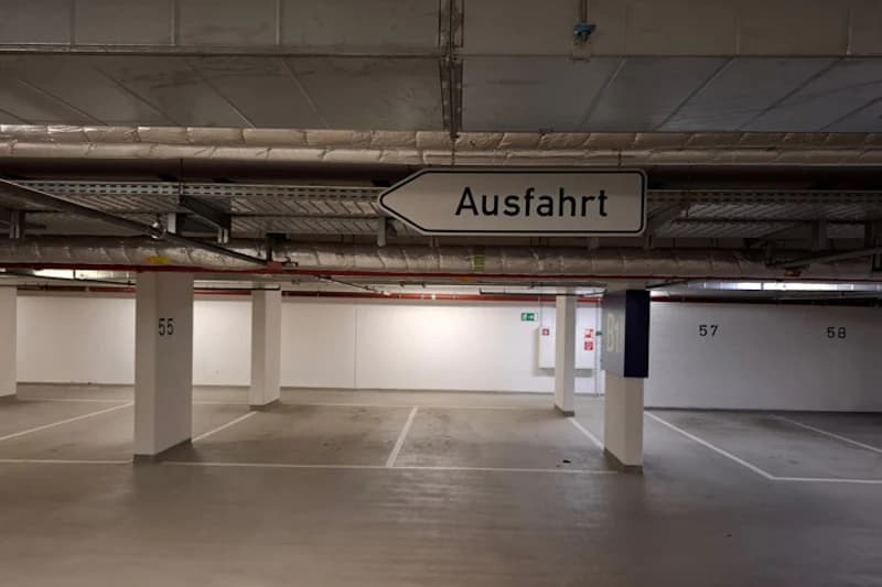 Leere Tiefgarage mit Pfeilschild Ausfahrt und markierten Stellplätzen Nummer 55 bis 58.
