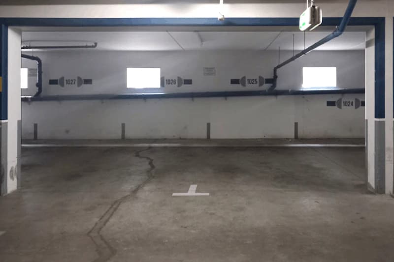 Leere Tiefgarage mit markierten Stellplätzen und Wandnummern 1024 bis 1027 sowie sichtbaren Rohrleitungen.