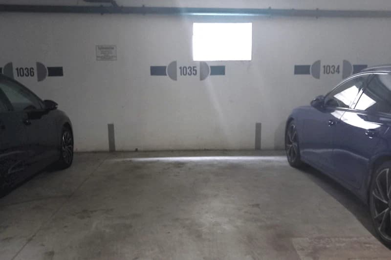 Leerer Tiefgaragenparkplatz Nummer 1035 zwischen geparkten Autos, Wand mit Fenster und Nummern 1034–1036.
