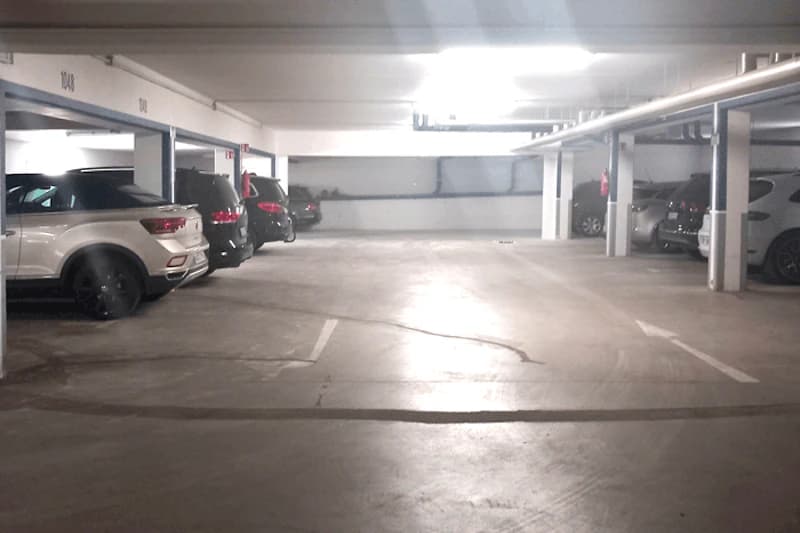 Beleuchtete Tiefgarage mit mehreren geparkten Autos und Betonstützen.