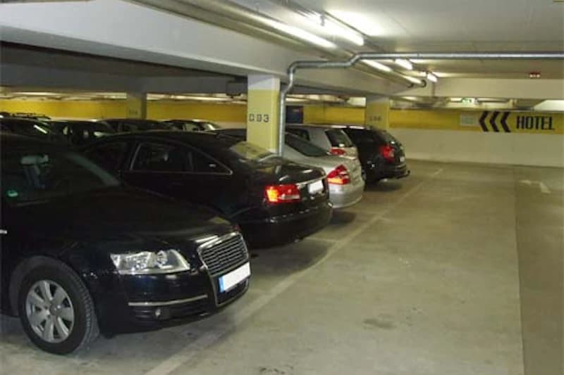Reihe geparkter Autos in beleuchteter Tiefgarage mit gelben Säulen und Hinweis Hotel an der Wand.