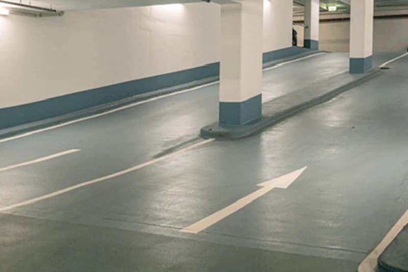 Leeres Parkhaus mit Pfeilmarkierung auf dem Boden, Säulen und gedämpfter Deckenbeleuchtung.